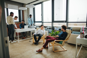 Canvas Print - Mixed race coworkers having rest after lunch, relaxing in office lounge zone, discussing common themes.