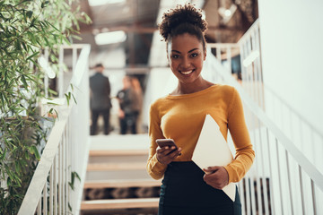 Joyful afro american businesswoman holding cellphone and documents