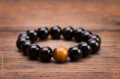 Fotomural Bracelet from round black stones lying on a wooden background.