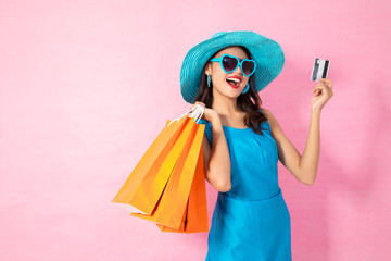 Portrait of a happy Asian pretty girl holding shopping bags while Hold Credit Cards and sunglasses looking away isolated over pink background,colorful shopping concept.