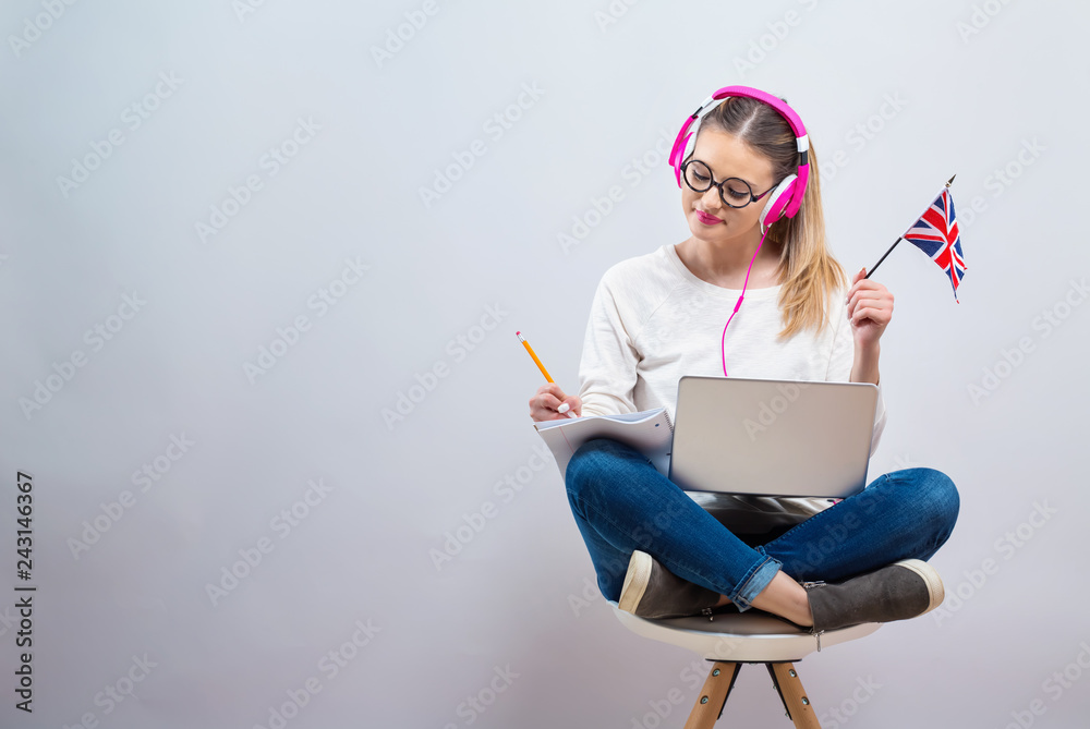 Young woman with UK flag using a laptop computer on a gray background - obrazy, fototapety, plakaty 