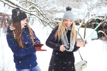 funny and happy two beautiful girlfriends play in the snow in winter, a lot of snow and winter clothes. blonde and brunette emotions