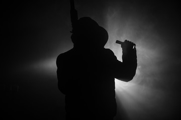 Silhouette of man with assault rifle ready to attack on dark toned foggy background or dangerous bandit in black wearing balaclava and holding gun in hand. Shooting terrorist with weapon theme decor