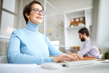 Wall Mural - Young designer or manager typing in front of computer screen while sitting by desk in working environment