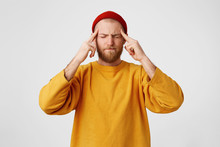 The Guy Holds Fingers On Temples, His Eyes Are Squinting, Trying To Remember Something. Bearded Man Feels Headache, Massages His Temples With Fingers, Isolated On A White Background.