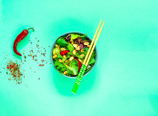 Wall Mural - Vegan Vegetable Salad with Peanuts in blue bowl with chopsticks on green background. Organic food concept. 