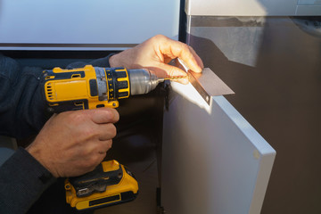 Wall Mural - Worker sets a new handle on the white cabinet with a screwdriver installing kitchen cabinets