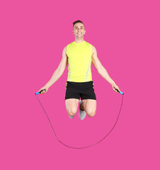 Wall Mural - Full length portrait of young sportive man training with jump rope on color background