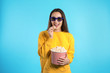 Woman with 3D glasses and popcorn during cinema show on color background