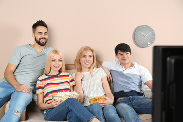 Poster - Young friends with snacks watching TV on sofa at home