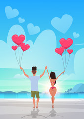 Wall Mural - rear view couple holding pink heart shape air balloons sea ocean beach summer vacation concept man woman in love over sunset seascape background full length vertical flat