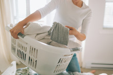 A Woman Folding Laundry In A Bright White Bedroom.