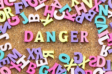 Poster - Color alphabet in word danger with another letter as frame on cork board background