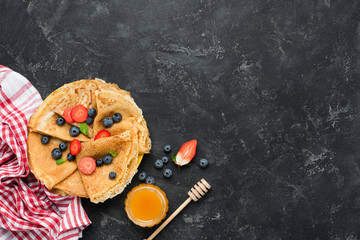 Wall Mural - Tasty homemade crepes with honey and berries on black concrete background. Table top view. Maslenitsa food