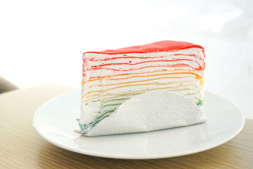 Wall Mural - Rainbow crape cake on white plate on wooden table..