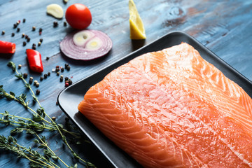 Plate with fillet of fresh salmon on wooden background, closeup