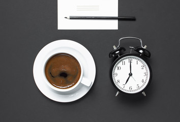 Flat lay cup of black coffee, black alarm clock, pencil, white cards on gray dark background top view copy space. Minimalistic food concept, morning breakfast, time to work hot drink coffee background