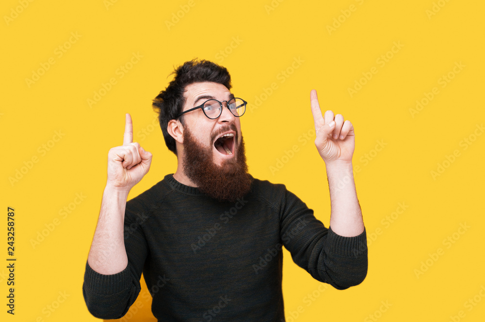 Portrait of amazed bearded man pointing up over yellow background - obrazy, fototapety, plakaty 