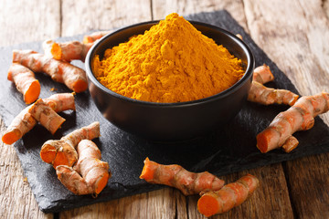 Wall Mural - Freshly ground turmeric in a black bowl and fresh root close-up. horizontal