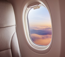 Airplane interior with window view of sunset above clouds.