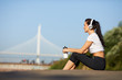 © pressmaster - Content beautiful fit young woman in sportswear sitting on ground and listening to music in headphones while relaxing after outdoor training