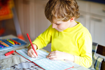 Happy smiling little kid boy at home making homework at the morning before the school starts. Little child doing excercise, indoors. Elementary school and education: Boy writing letters and numbers