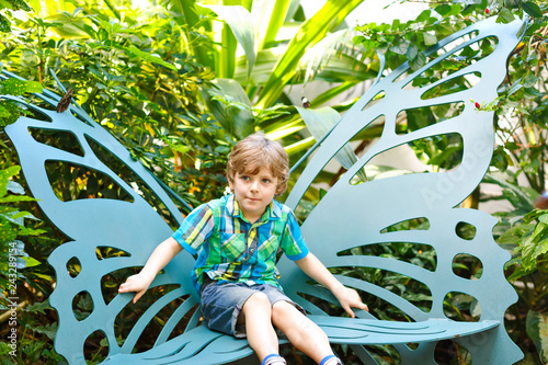 Foto Little blond preschool kid boy discovering flowers and butterflies at botanic garden
