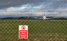 Restricted Area Sign On Fence Of Airport Runway, Passenger Aircraft Taxiing On Runway In The Background