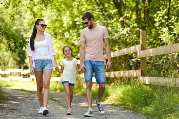 Wall Mural - family, leisure and people concept - happy mother, father and little daughter walking in summer park