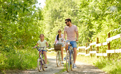 family, leisure and people concept - happy mother, father and little daughter riding bicycles in sum