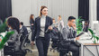 © LIGHTFIELD STUDIOS - smiling young businesswoman holding folder with papers and looking at coworkers while walking in office