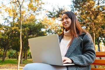 Sticker - Smiling young asian woman wearing coat sitting on a bench