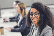 © LIGHTFIELD STUDIOS - beautiful young african american woman in headset smiling at camera while working with colleagues in office