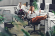 © LIGHTFIELD STUDIOS - beautiful young businesswoman holding cup and using smartphone while sitting with legs on desk in open space office