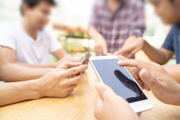 group of young man or friends playing online application game in modern touch screen mobile on wood table.