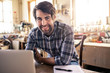 © mavoimages - Woodworker smiling while using a laptop in his workshop