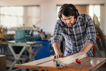 Wall Mural - Carpenter sawing wood with a table saw in his workshop