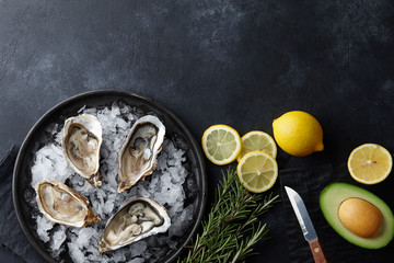 Wall Mural - Fresh opened oysters in a plate with ice and lemon on black textured background, top view