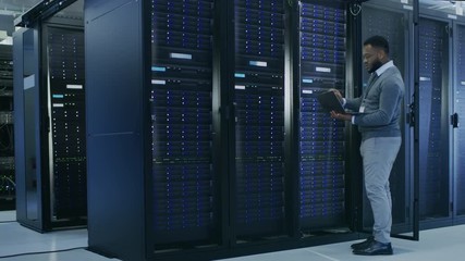 Aufkleber - Black IT Specialist is Working on Laptop in Data Center while Standing Before Server Rack. Running Diagnostics, Putting in Data or Doing Maintenance Work.