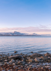 Wall Mural - View of rocky shoreline, lake, and snow covered mountains at sunset