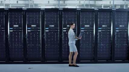 Poster - Female Data Center IT Engineer Walking Through Server Rack Corridor with a Laptop Computer. She is Visually Inspecting Working Server Cabinets.