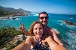 happy couple taking selfie photo in front of the sea in Tayrona National Park, Tropical Colombia. Crazy tourists travelling on the white beach of caribbean sea. 