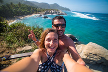 Happy Couple Taking Selfie Photo In Front Of The Sea In Tayrona National Park, Tropical Colombia. Crazy Tourists Travelling On The White Beach Of Caribbean Sea. 