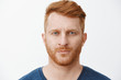 © Cookie Studio - Close-up shot of serious-looking handsome adult european man with red hair and beard staring at camera with focused and determined expression, standing in strict pose over gray background