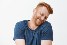 Silly And Funny Caucasian Redhead Guy With Bristle, Tilting Head And Leaning On Shoulder With Lovely And Cute Expression, Smiling With Closed Eyes Being Tender And Girly Over Gray Background
