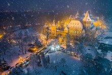 Budapest, Hungary - Christmas Market In Snowy City Park (Varosliget) From Above At Night With Snowy Trees And Vajdahunyad Castle