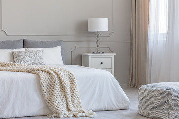 Beige woolen blanket on white duvet on king size bed in elegant bedroom interior