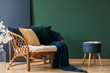 © Photographee.eu - Dark blue pouf with open book next to rattan settee with pillows and blanket, copy space on the empty and blue grey wall