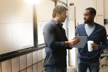 Colleagues standing together in modern office going over ideas on tablet