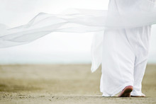 Photo Of A Man Walking In A White Robe On The Sand. A Picture From The Back, A Person Is Visible To The Waist, Clothes Are Fluttering In The Wind